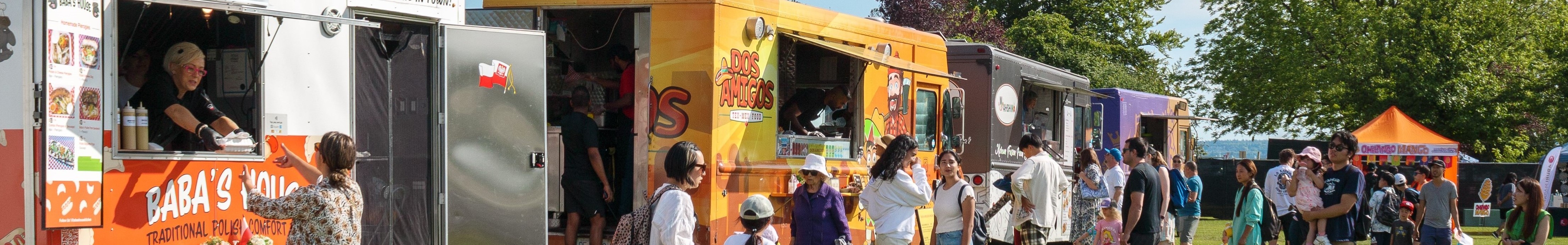 The image shows a group of people walking around a food truck. The food truck appears to offer traditional Polish comfort food. The setting is an outdoor international lounge with food trucks from different countries.