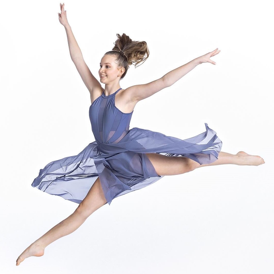 The image features a person wearing a blue dress, likely a dancer performing a choreographed routine. The photo showcases elements of dance and ballet, including balance, movement, and grace. The individual appears to be a ballet dancer based on the attire and posture.