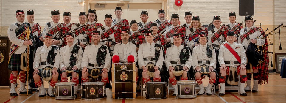 The J.P. Fell Pipe Band posing for a group photo, wearing traditional Scottish attire.