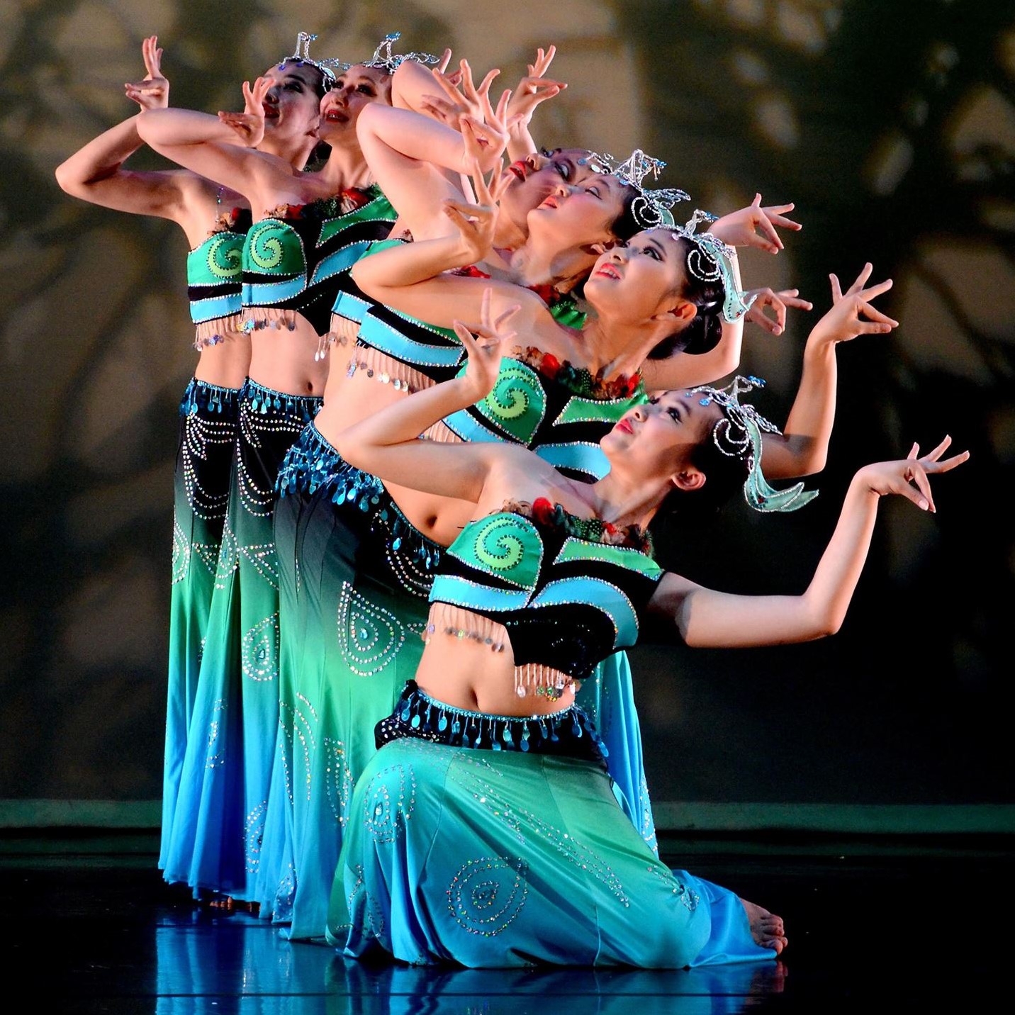 The photo depicts a group of women from the Lorita Leung Dance Academy dancing and making poses with their hands. They are dressed in dance attire and are likely performing choreographed routines from various dance styles such as modern dance or belly dance.