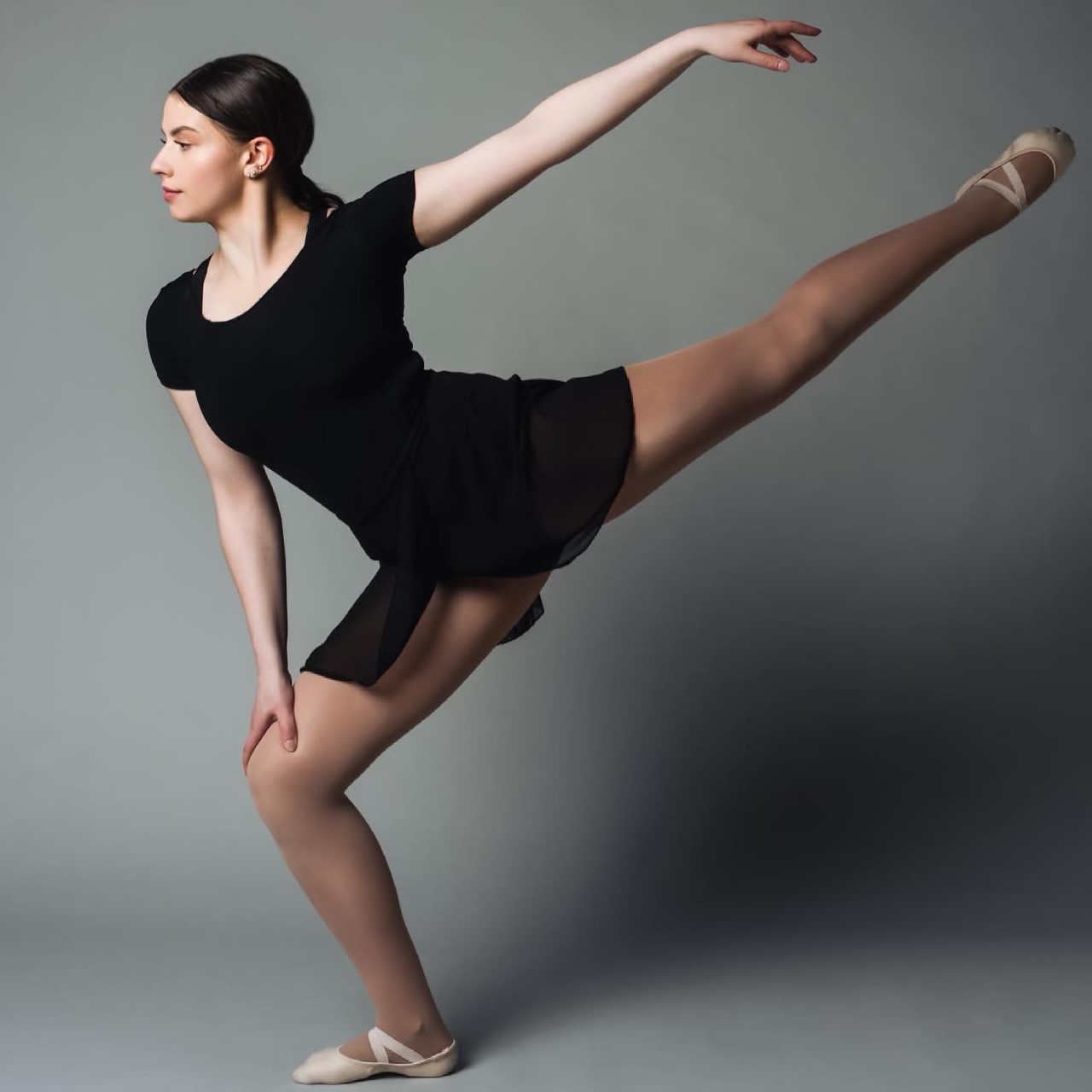 The photo shows a woman in a black dress, likely a ballet dancer, practicing her choreography. She is demonstrating balance and precision in her movements. The image is likely taken at Perform Art Studios.