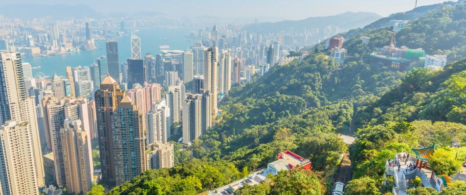 The image shows an aerial view of Victoria Peak in Hong Kong, with many tall buildings in the cityscape. The view includes the popular Peak Tram and Lion's Pavilion terrace.