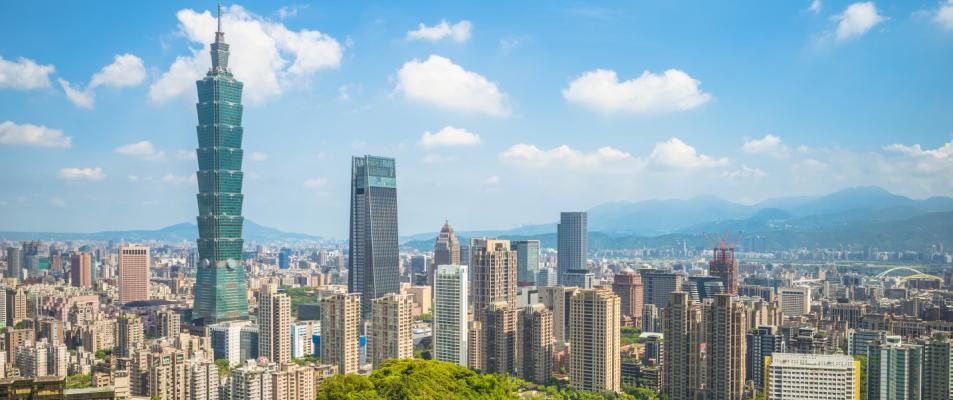 The photo is of a cityscape in Taiwan featuring tall buildings against a backdrop of clouds and sky. The urban area includes skyscrapers and tower blocks, creating a metropolitan landscape.