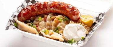 A white container filled with a sausage, perogies, and sour cream.