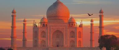 The photo shows a large building with a domed roof in the foreground, with the Taj Mahal in the background during sunset. It is a beautiful scene capturing the historic and architectural significance of the two structures.