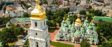 The image is of a large building with a gold-domed roof surrounded by trees. It is a cathedral in Ukraine known as St. Sophia's Cathedral in Kiev, as seen from the height of St. Sophia's Square in the cityscape.